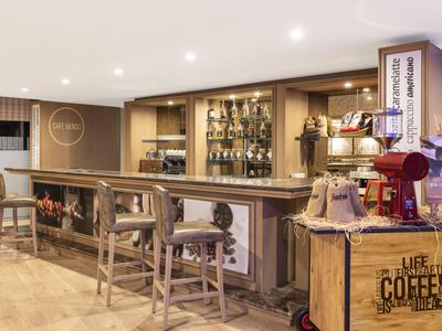 Gemütliche Bar mit Holztheke, Barhockern, Regalen voller Flaschen und einem Kaffeewagen rechts.