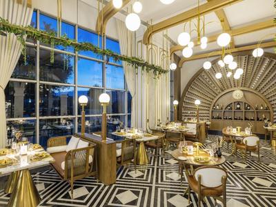 Elegantes Restaurant mit geometrischem schwarz-weißem Bodenmuster, goldenen Elementen und großen Fenstern.