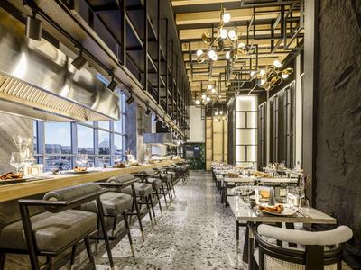 Modernes Restaurant mit langem Fenster, hohen Decken, bequemen Stühlen und eleganten Tischen.