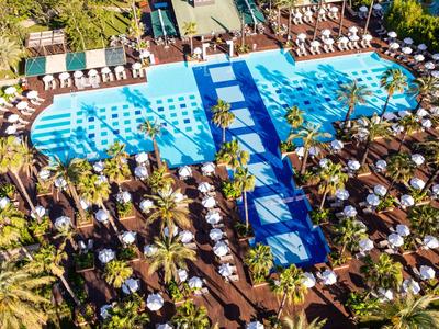 Velká bazénová oblast s lehátky, slunečníky a obklopujícími palmami v resortu.