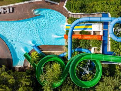 Wasserpark mit großen grünen und blauen Wasserrutschen über einem Pool und umgeben von Bäumen.