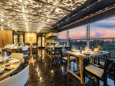 Elegantes Restaurant mit Holzdecke, schwarzen Möbeln und Panoramafenster bei Sonnenuntergang.