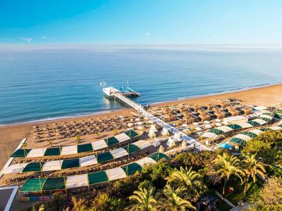 Langer Steg führt über den Sandstrand ins ruhige blaue Meer bei klarem Himmel.
