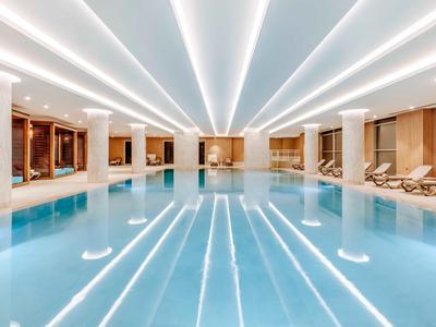 Moderní vnitřní bazén s bílými sloupy a lehátky v elegantním hotelu.