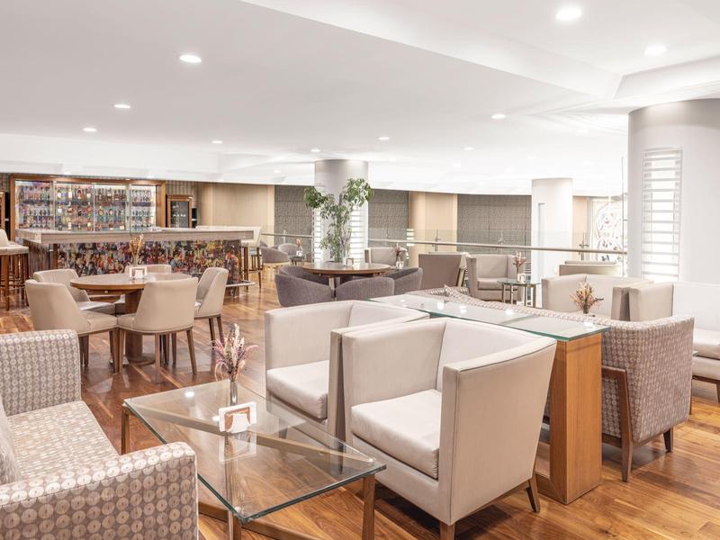 Helles, modernes Café mit Holzboden, weißen Sesseln, Tischen und Bücherregal im Hintergrund.