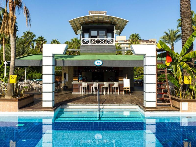 Moderner Pool mit blauem Wasser, umgeben von Palmen und einer weißen, offenen Lounge.