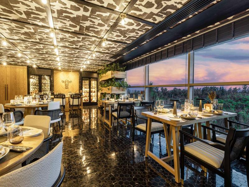 Elegantes Restaurant mit Holzdecke, schwarzen Möbeln und Panoramafenster bei Sonnenuntergang.