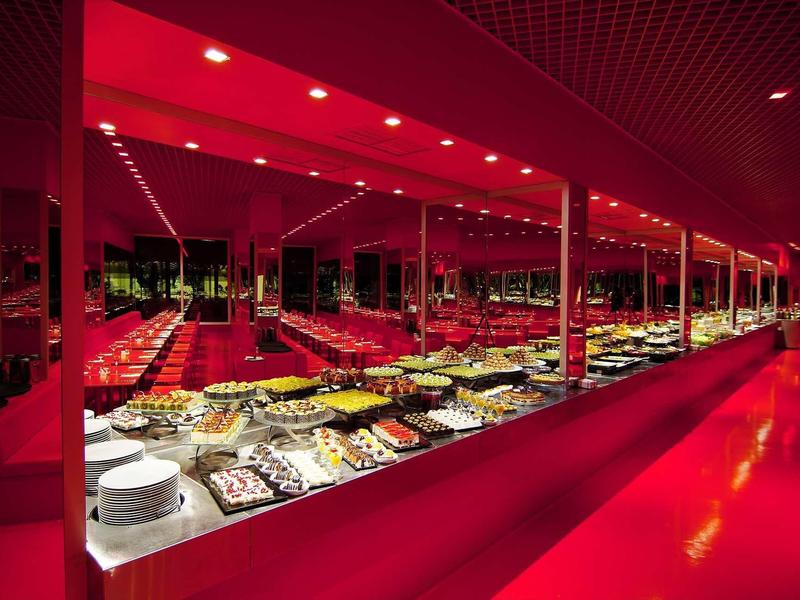 Buffet mit vielfältigen Speisen in modernem, rot beleuchtetem Raum mit langen Spiegelwänden.