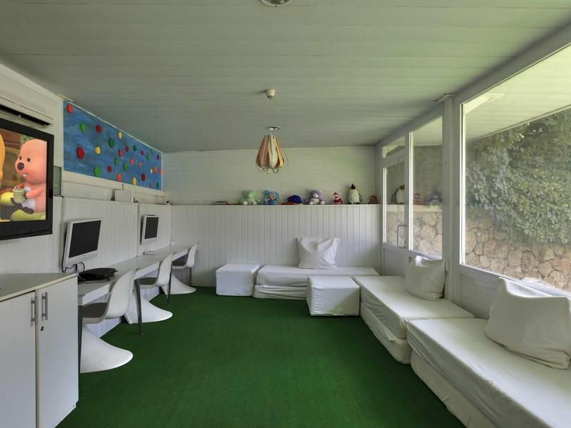 Moderner Raum mit weißen Möbeln, grüner Teppichboden und großen Fenstern mit Blick ins Freie.