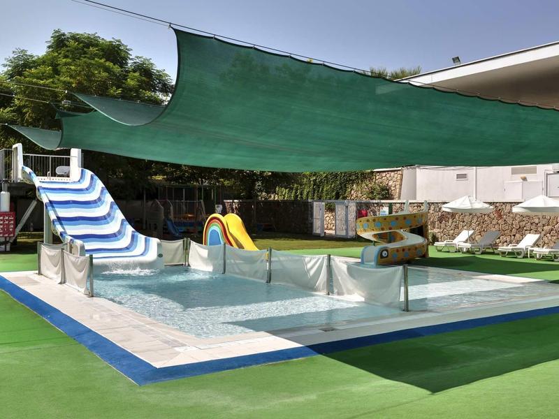 Outdoor-Pool mit mehreren bunten Wasserrutschen, grünem Sonnensegel und grünem Kunstrasen.