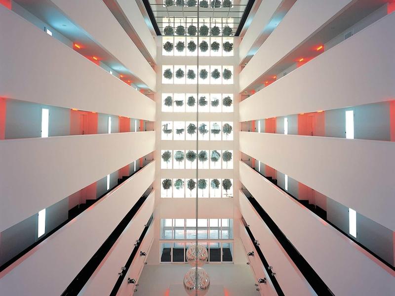 Blick nach oben in ein modernes Atrium mit weißen Wänden, symmetrischen Balkonen und Beleuchtung.