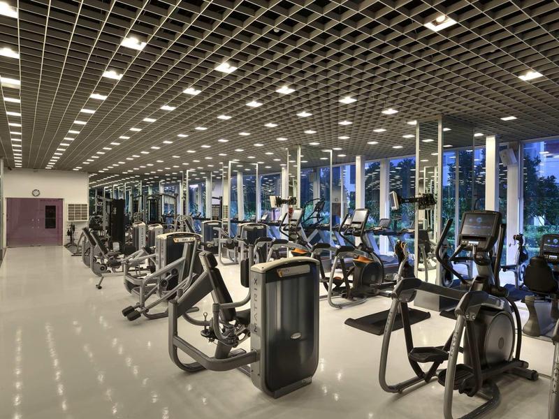 Großer Fitnessraum mit modernen Trainingsgeräten, elliptischen Maschinen und breiten Fenstern am Abend.