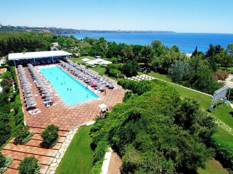Großer rechteckiger Pool mit Liegestühlen, umgeben von grünen Gärten und Blick auf das blaue Meer.