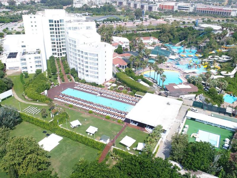 Großer Hotelkomplex mit mehreren weißen Gebäuden, Pools, grünen Gärten und umliegender Stadtlandschaft.