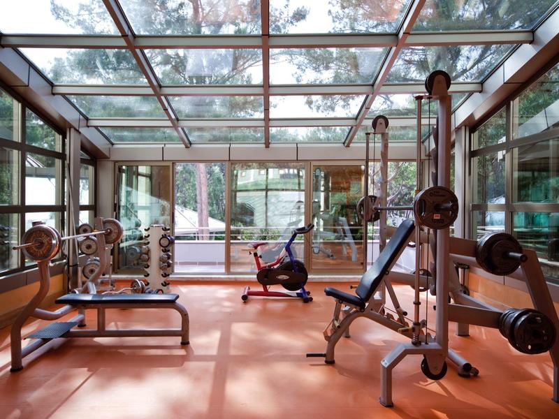 Moderner Fitnessraum mit großen Fenstern, Glasdecke, Hantelbänken und Station für Krafttraining.