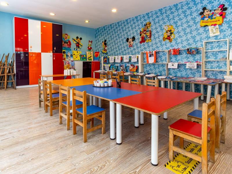 Farbenfroher Kinderspielraum mit kleinen Holztischen, Stühlen und Disney-Wandbildern.