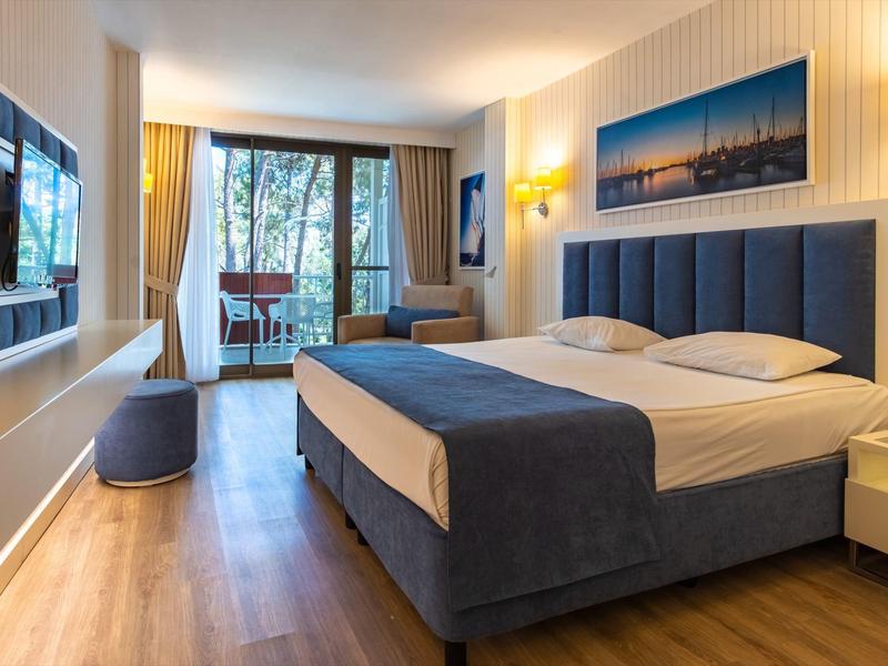 Modernes Hotelzimmer mit Doppelbett, Holzfußboden, Balkon und Fernseher an der Wand.