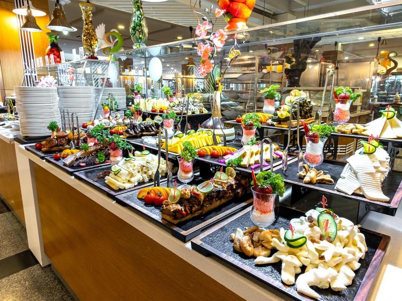 Buntes Buffet mit frischem Obst, Gemüse, Sandwiches und dekorativen Pflanzen in hellem Raum.