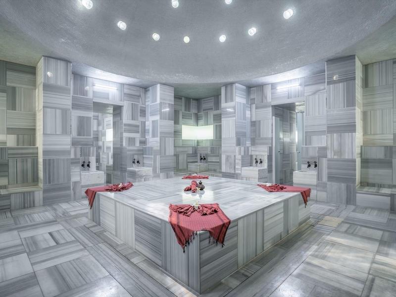 Großer türkischer Hamam mit grauen Marmorwänden, quadratischem Becken und roten Tüchern.