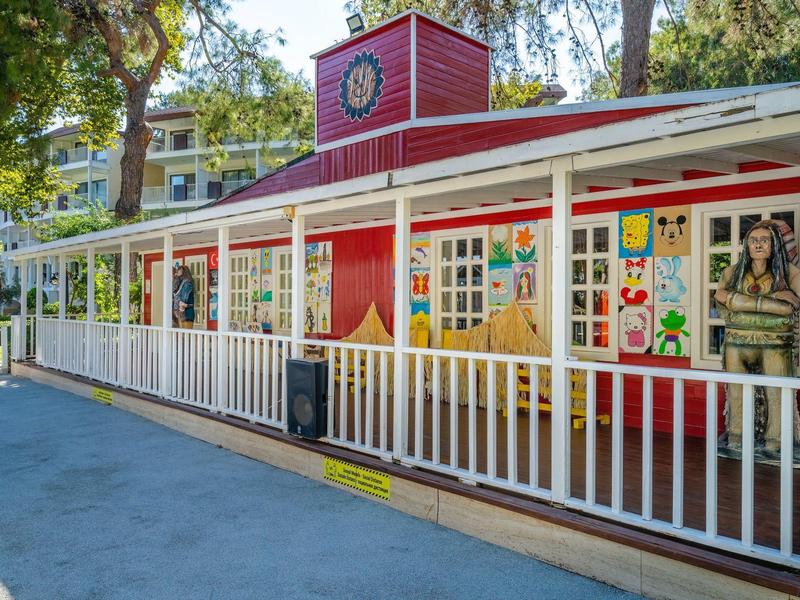 Bunte Grundschule mit roten Wänden, vielen Fensterbildern und weißem Zaun im sonnigen Innenhof.