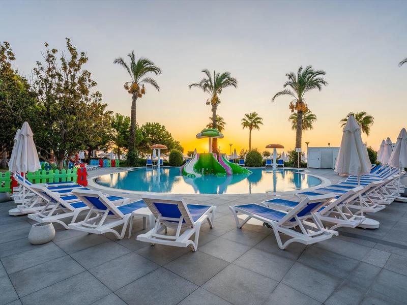 Pool mit Sonnenliegen, weißen Schirmen und Palmen im Hintergrund bei Sonnenuntergang.