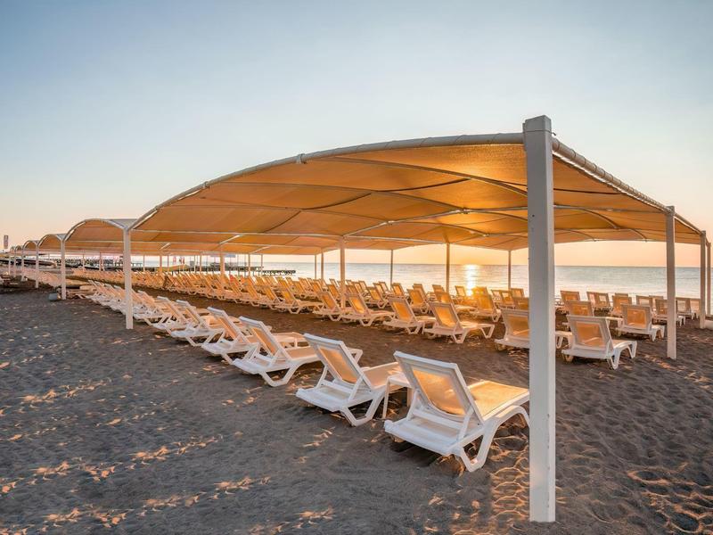 Strand mit weißen Liegestühlen unter einem großen Sonnensegel bei Sonnenuntergang.