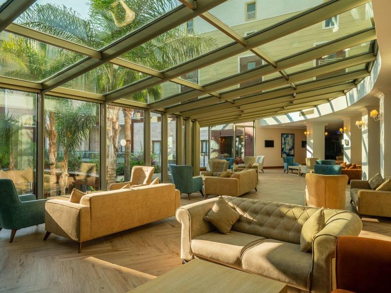 Heller Wintergarten mit großen Glaswänden, bequemen Sofas, Sesseln und Holzboden.