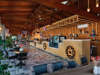 Przytulny bar hotelowy z drewnianym sufitem, stołami i krzesłami, roślinami i nowoczesnym oświetleniem.