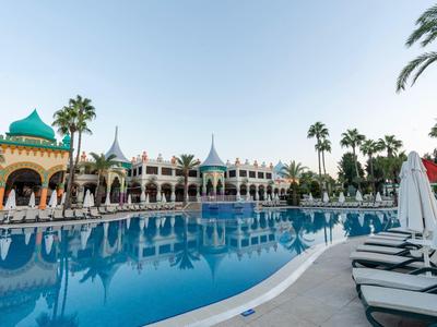 Grande piscina davanti a un hotel con lettini e palme sotto un cielo sereno