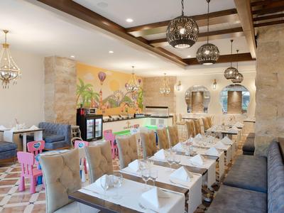 Elegancka restauracja z długim nakrytym stołem, wygodnymi krzesłami i dekoracyjnym malowidłem na ścianie.