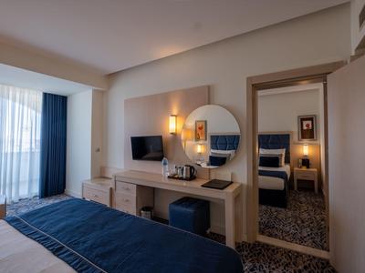 Modern eingerichtetes Hotelzimmer mit Schreibtisch, Spiegel und Zugang zu einem angrenzenden Raum.