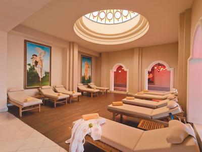 Jasne pomieszczenie wellness z leżakami, delikatnym oświetleniem i ozdobnymi obrazami na ścianach.