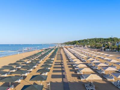 Szeroka piaszczysta plaża z rzędami parasoli i leżaków pod bezchmurnym niebem