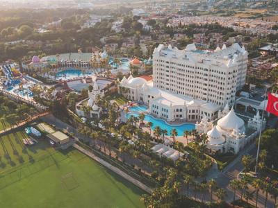 Widok z lotu ptaka na duży ośrodek z kilkoma basenami i białym budynkiem hotelowym obok boiska do piłki nożnej.