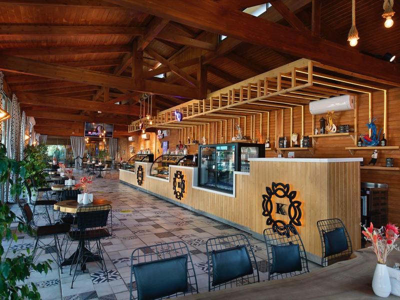 Przytulny bar hotelowy z drewnianym sufitem, stołami i krzesłami, roślinami i nowoczesnym oświetleniem.