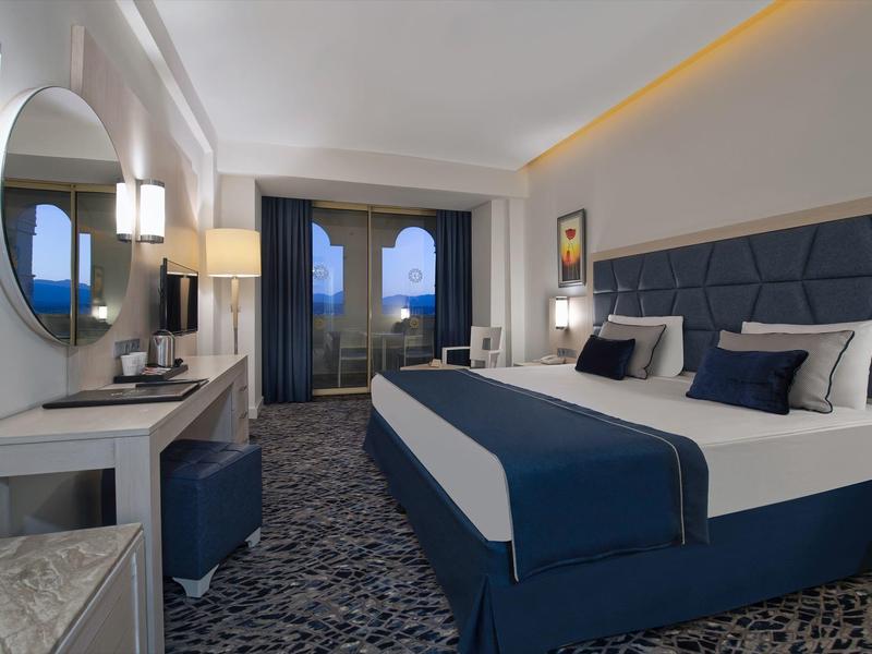 Nowoczesny pokój hotelowy z dużym łóżkiem, niebiesko-białym wystrojem i balkonem z widokiem na zewnątrz.