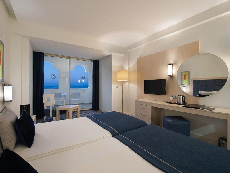 Nowoczesny pokój hotelowy z dwoma pojedynczymi łóżkami, biurkiem, okrągłym lustrem i tarasem z widokiem na morze.