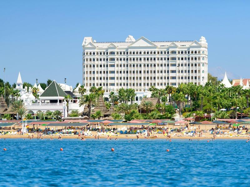 Duży hotel przy plaży z wieloma palmami i czystym niebieskim morzem na pierwszym planie