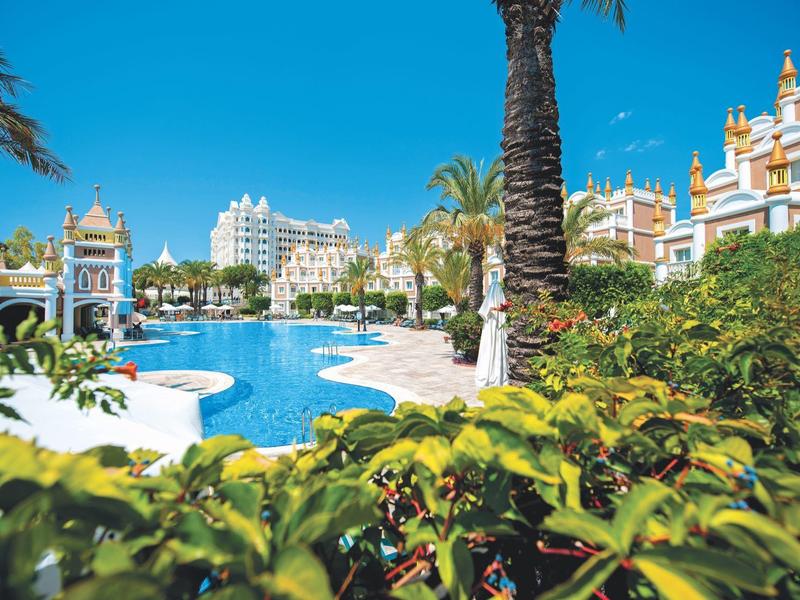 Duży basen hotelowy z palmami i zadbanymi ogrodami pod niebieskim niebem