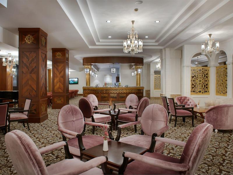 Elegancki salon hotelowy z różowymi aksamitnymi krzesłami, żyrandolami i dywanem.