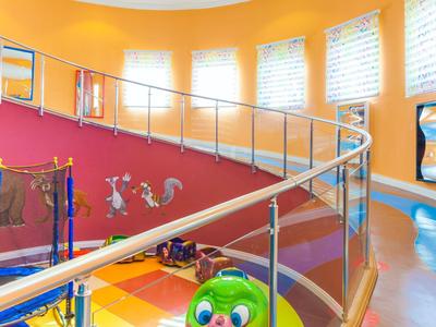 Área de juegos infantil luminosa con suelo colorido y juguetes de animales en espacio moderno con escalera curva.