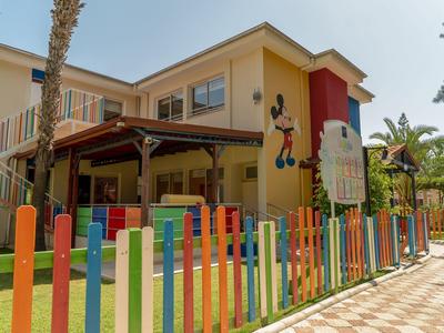 Zona infantil frente a un hotel colorido con palmeras y un gran dibujo animado de ratón.