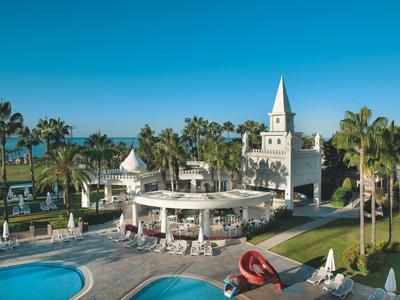 Complejo hotelero con piscina, palmeras y torre en un entorno tropical soleado junto al mar.