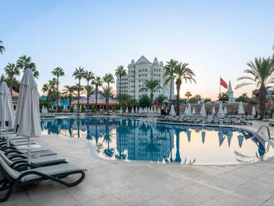 Gran piscina de hotel rodeada de palmeras y tumbonas bajo un cielo despejado.