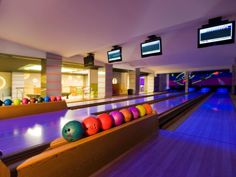 Pista de bolos moderna con bolas de colores y varias pistas en una sala iluminada cálidamente.