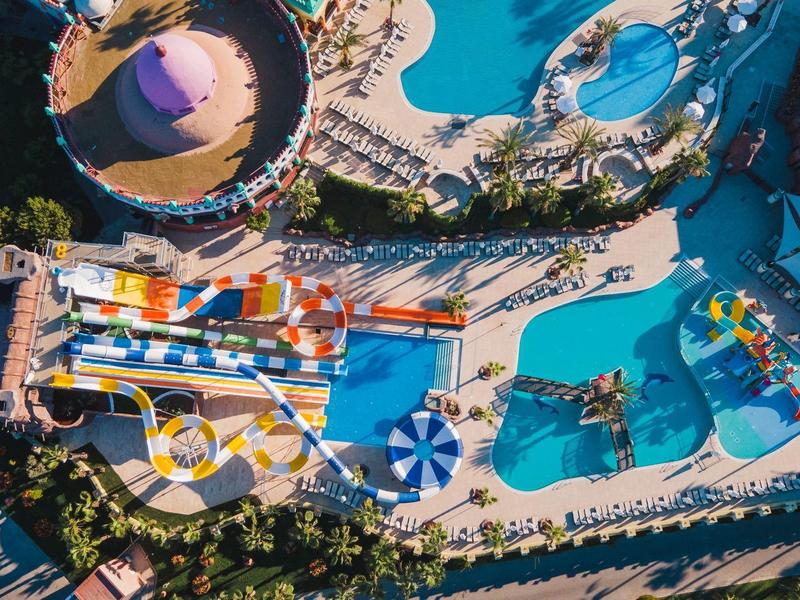 Vista aérea de una piscina de hotel concurrida con tumbonas y sombrillas coloridas.