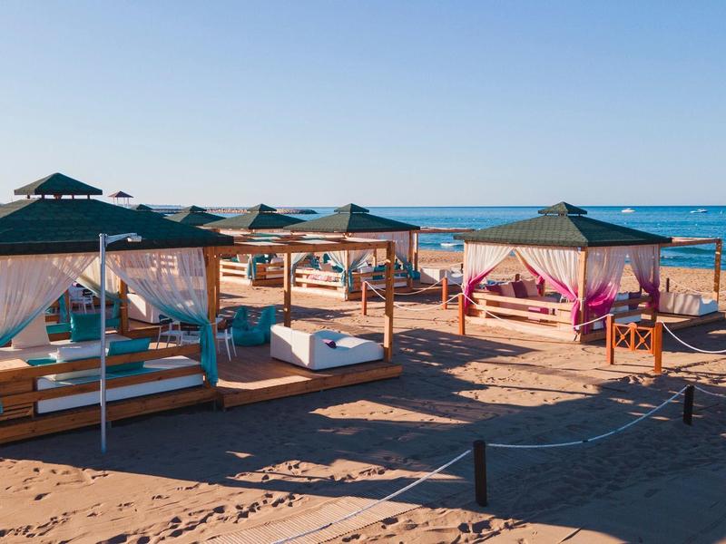 Playa con camas de día cómodas bajo pabellones y vista al mar azul tranquilo bajo cielo despejado.