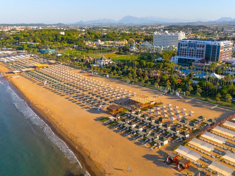 Larga playa de arena con sombrillas y hoteles al fondo en la costa.