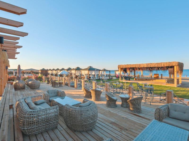 Área abierta de madera con muebles junto a un restaurante de playa con vista al mar.