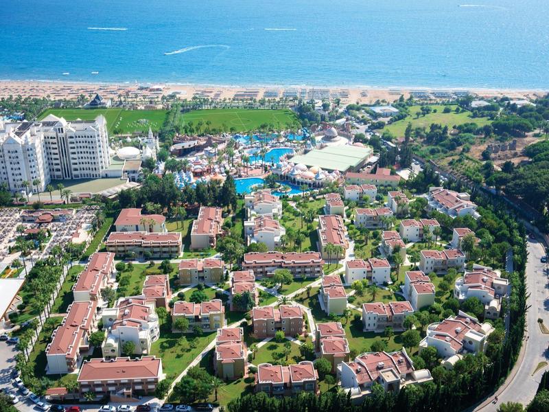 Vista aérea de un complejo vacacional con varios edificios, piscina y playa junto al mar.